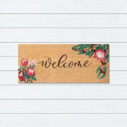 Doormat with floral design and 'Welcome' text on a white wooden background