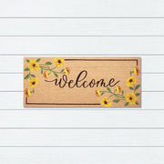 Doormat with 'Welcome' text and floral designs on a white wooden background